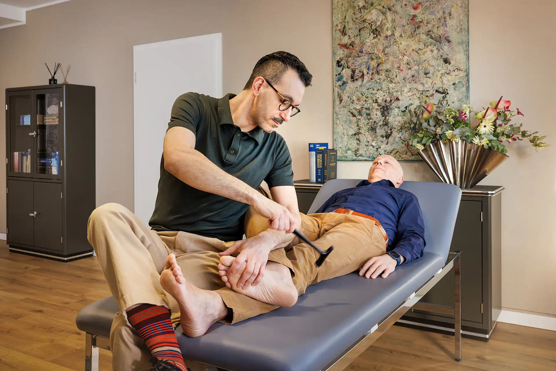 Arzt untersucht Beinreflex eines Patienten auf Behandlungsliege