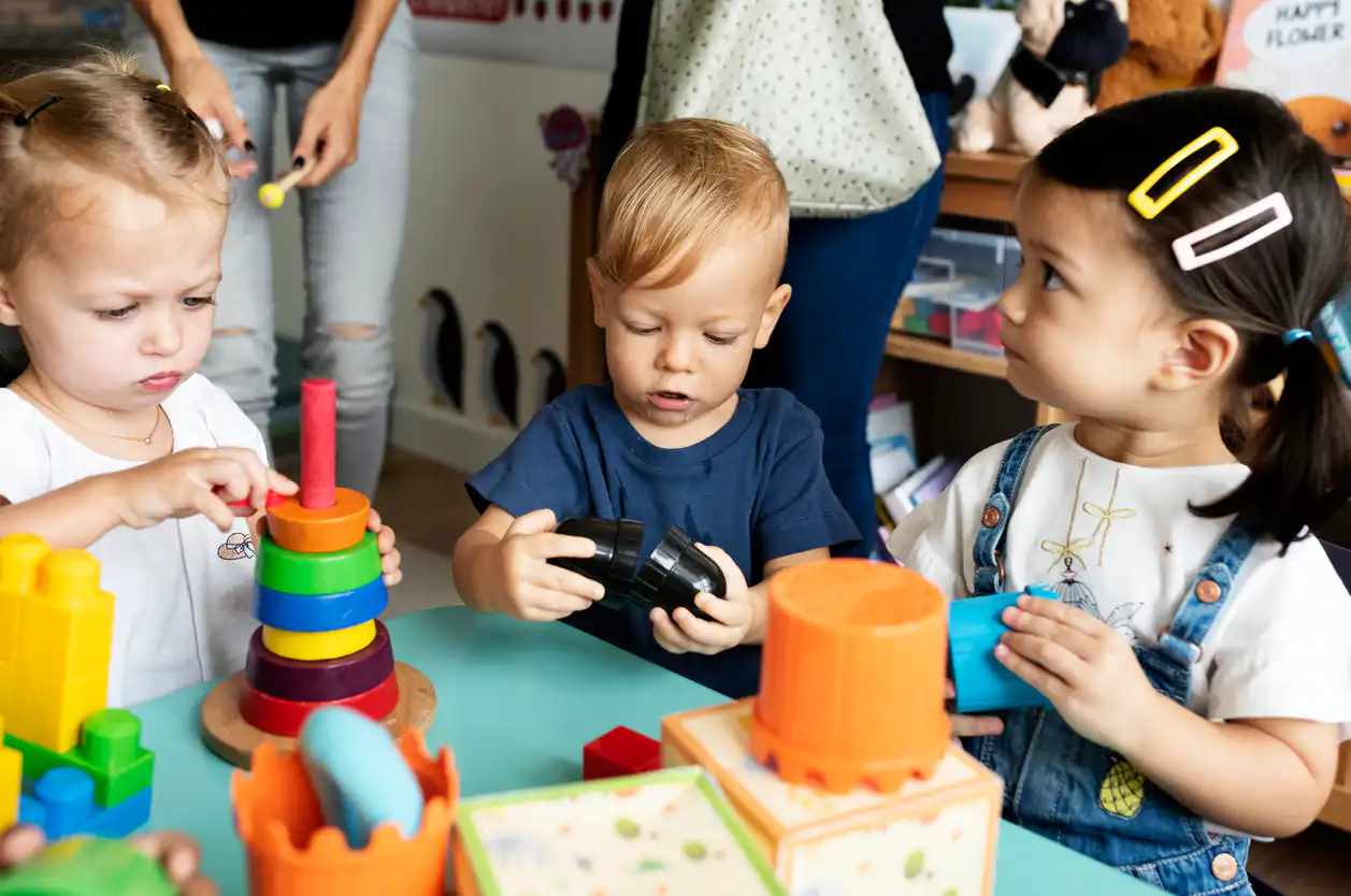 Drei Kleinkinder spielen mit bunten Bauklötzen am Tisch
