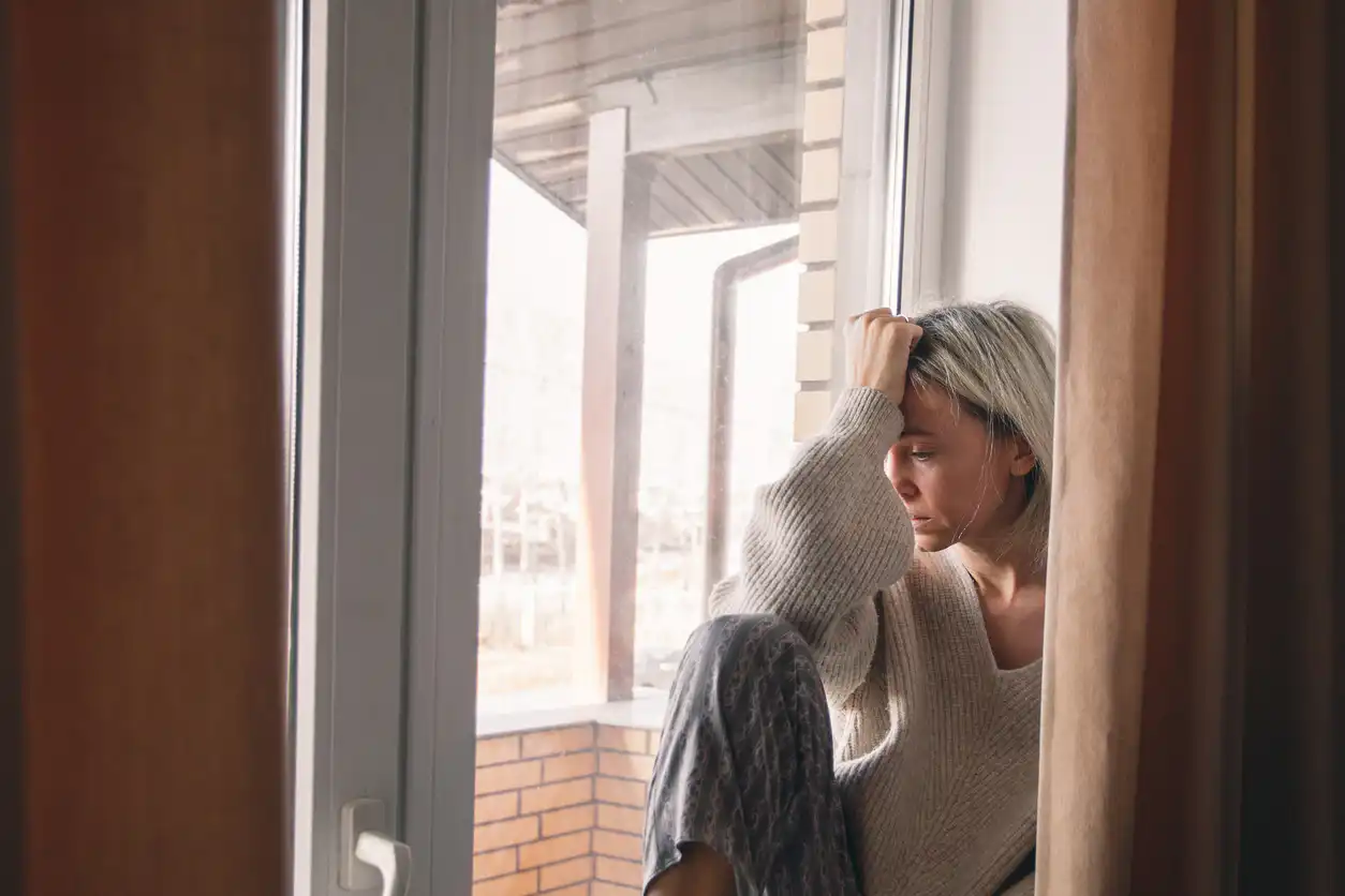 Traurige Frau sitzt nachdenklich am Fenster