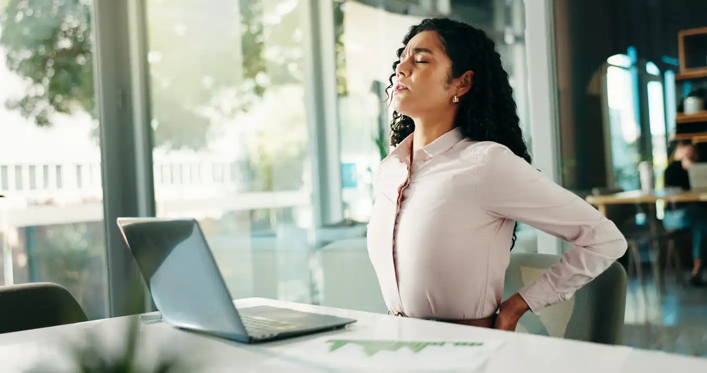 Frau im Büro dehnt Rücken am Laptop