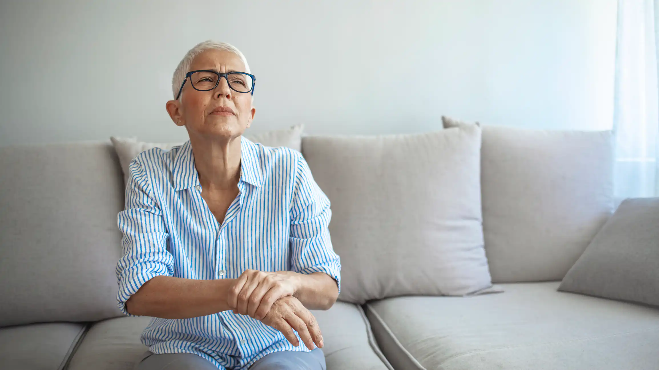 Ältere Frau mit Handgelenkschmerzen auf Sofa